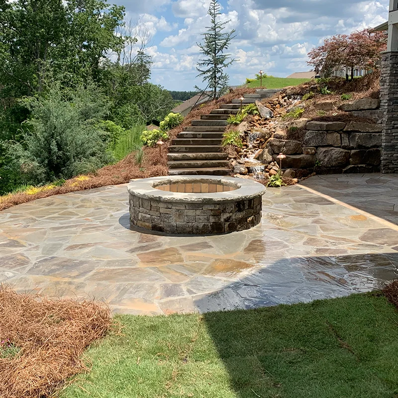a fire pit in the back yard of a home with rock stairs going down to it